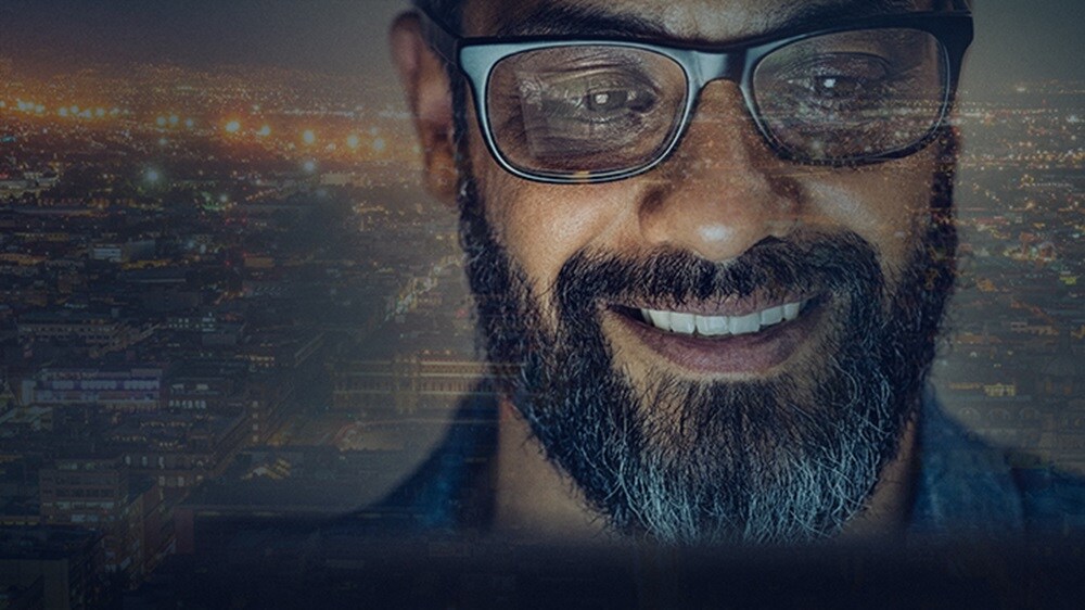 Carriere Tech in Maersk - Un dipendente sorridente con una città illuminata di notte sullo sfondo.