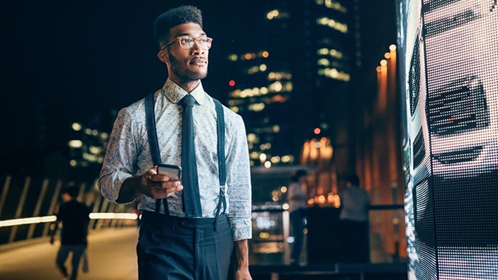 A man stands, holding a mobile phone, while gazing at something.