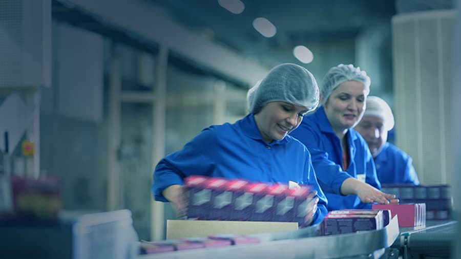 A group of workers arranging FMCG items on a conveyor belt in a distribution centre.