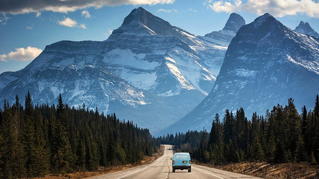 Van on long mountain road driving towards the mountains
