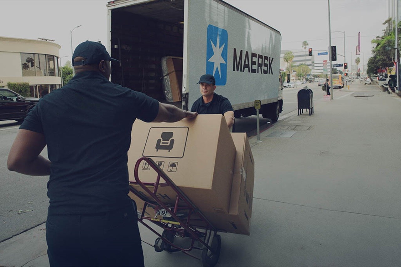 Workers unloading Maersk delivery truck on a city sidewalk.