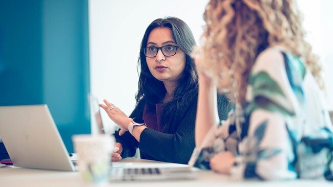 Two women talking at a table with open laptops