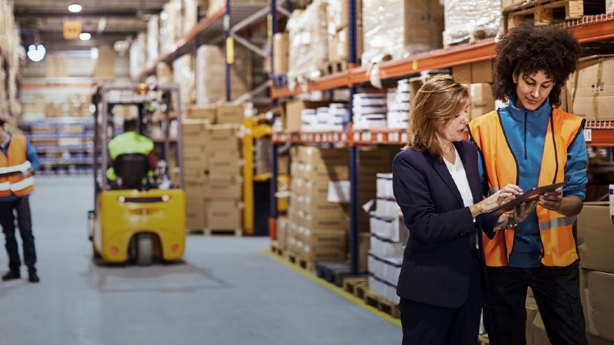 Two women working on a tablet in a warehouse