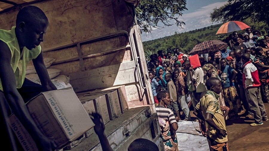 Men unloading a truck containing relief materials; people queuing up at the distribution centre.