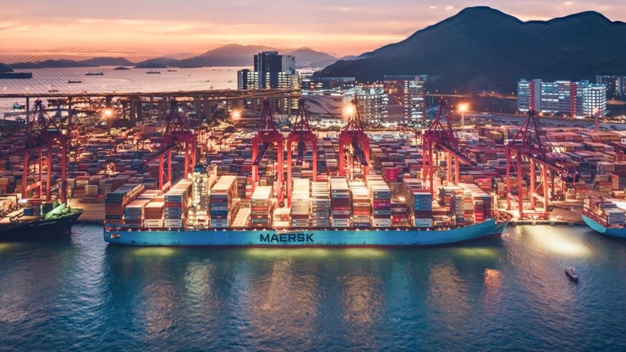 A large container Maersk ship docked in the harbor during dusk, with a colorful sky reflecting on the water's surface.