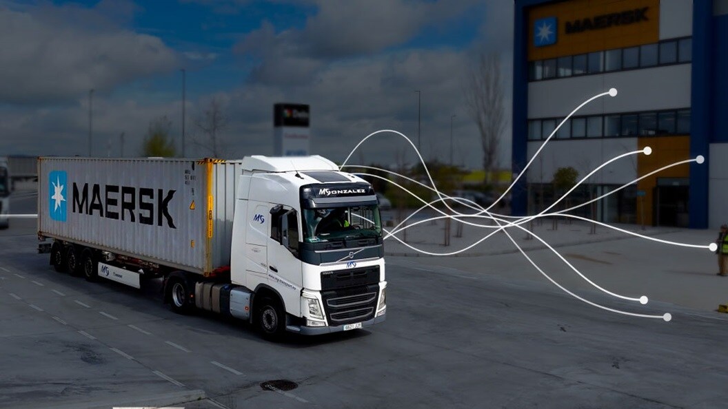 A truck drives down the road with a large building visible in the background.