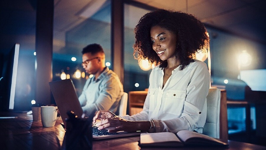 Two professionals working late at their computers in a modern, warmly lit office.
