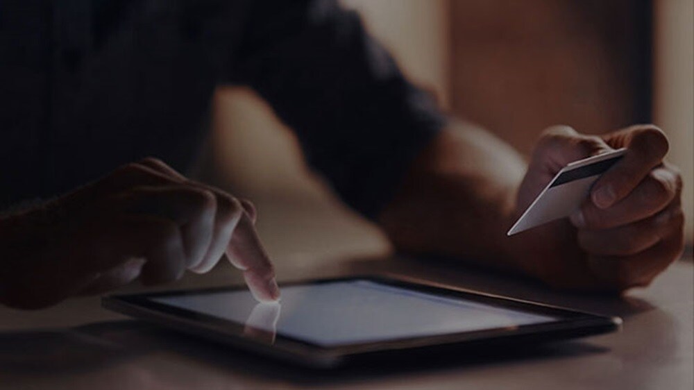 Nahaufnahme der Hand einer Person, die mit ihrer Kreditkarte auf einem Tablet eine Online-Zahlung vornimmt.