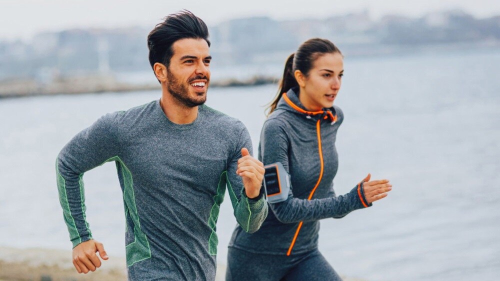 A man and woman running side by side on a sandy beach.