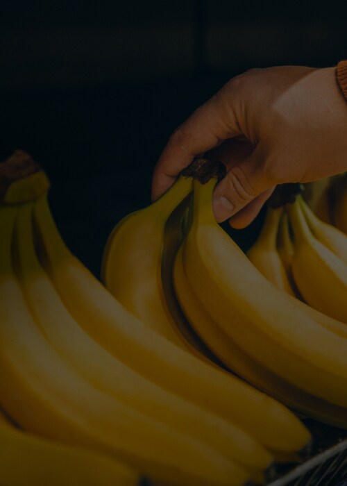 Hand selecting fresh bananas in a grocery store produce section