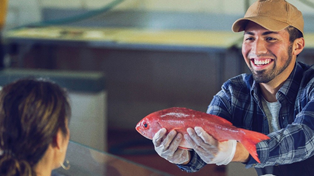 Refrigerated cargo – A smiling man holding a fish and showing it to a woman in a supermarket.