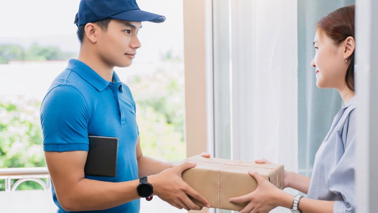 Delivery courier handing over a package to a smiling customer at home, representing last-mile logistics and customer satisfaction
