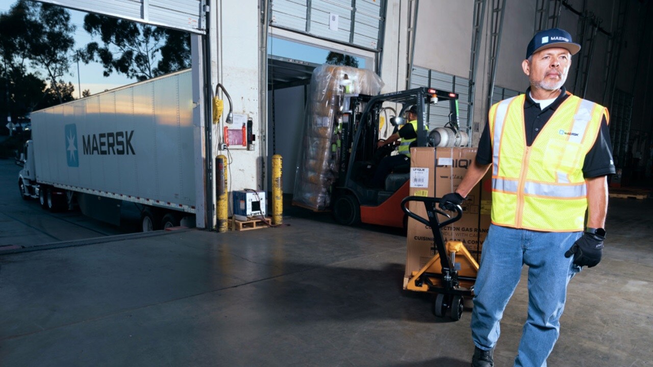 Employés d’entrepôt conduisant un chariot élévateur, chargeant des cartons d’expédition sur une palette en bois dans un camion porte-conteneur Maersk.