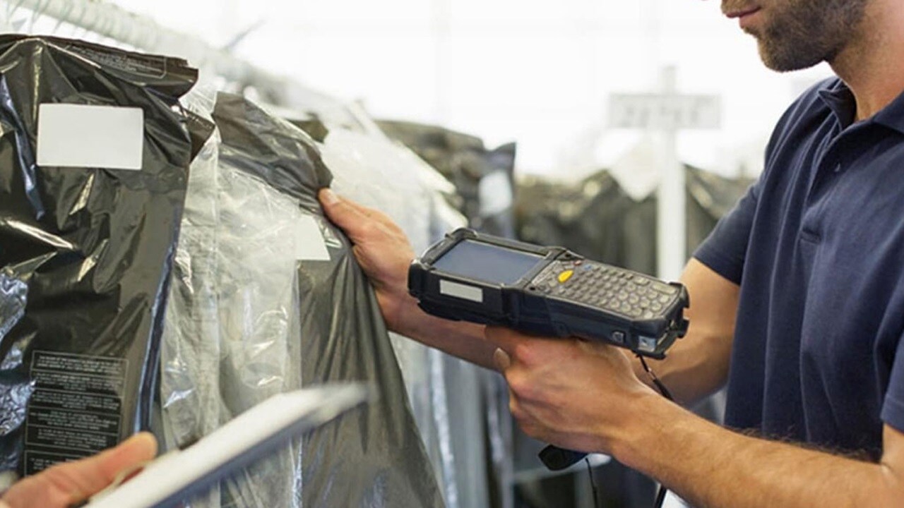 Trabalhador usa um scanner portátil para ler o código de barras em cada peça de vestuário a ser embarcada.